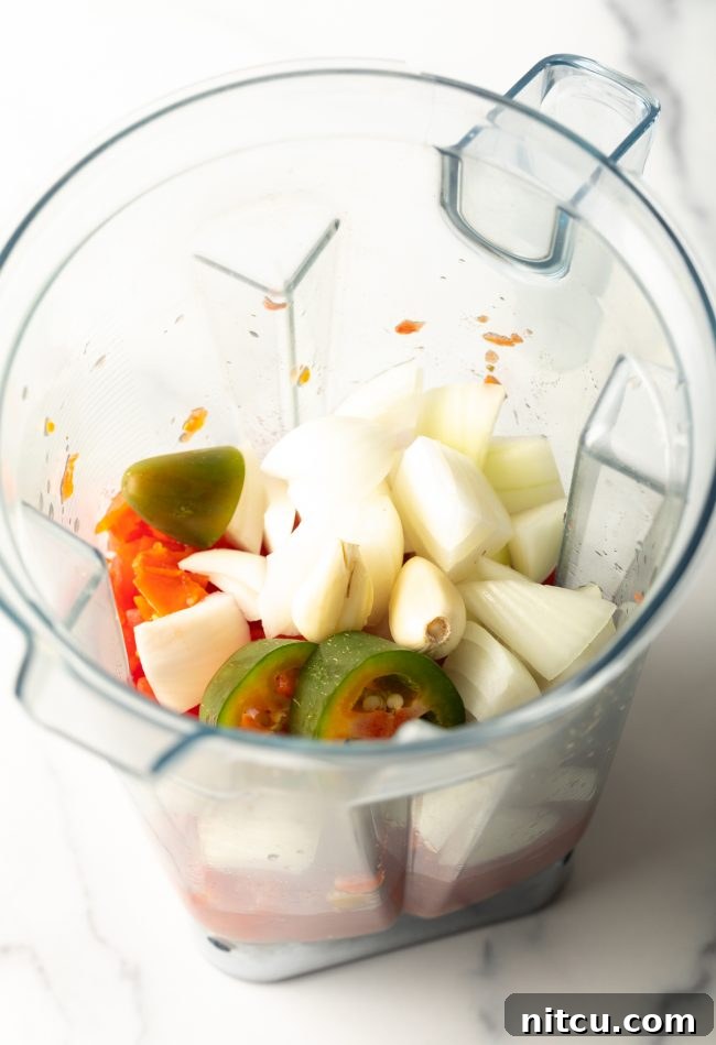 top view of a blender jar filled with diced tomatoes, chopped onion, jalapeño, and garlic, ready for blending