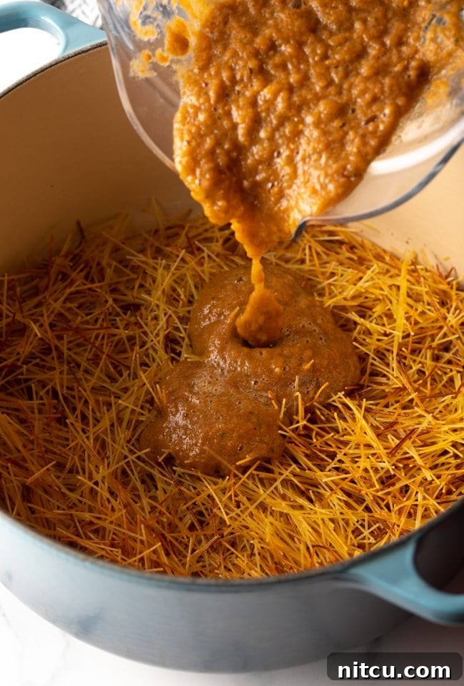 pouring vibrant tomato puree from a blender jar into a large pot with browned fideo pasta noodles