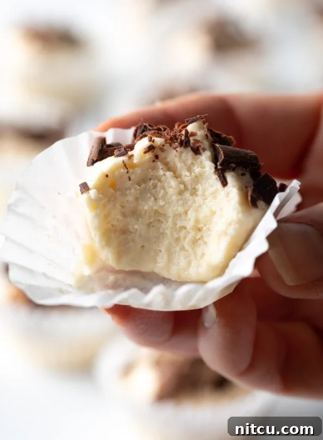 A hand holds a single keto cream cheese fat bomb, still in its paper liner, with a bite taken out, revealing the creamy texture, showcased up close.