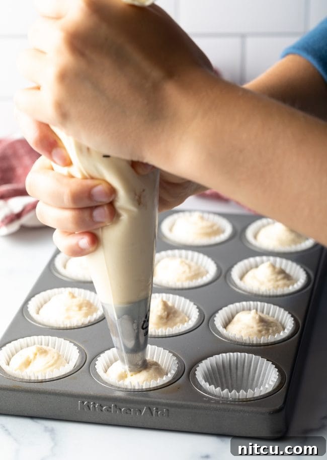 Hands using a piping bag to precisely pipe the low-carb keto cheesecake mixture into individual mini muffin pan liners for a clean and elegant presentation.