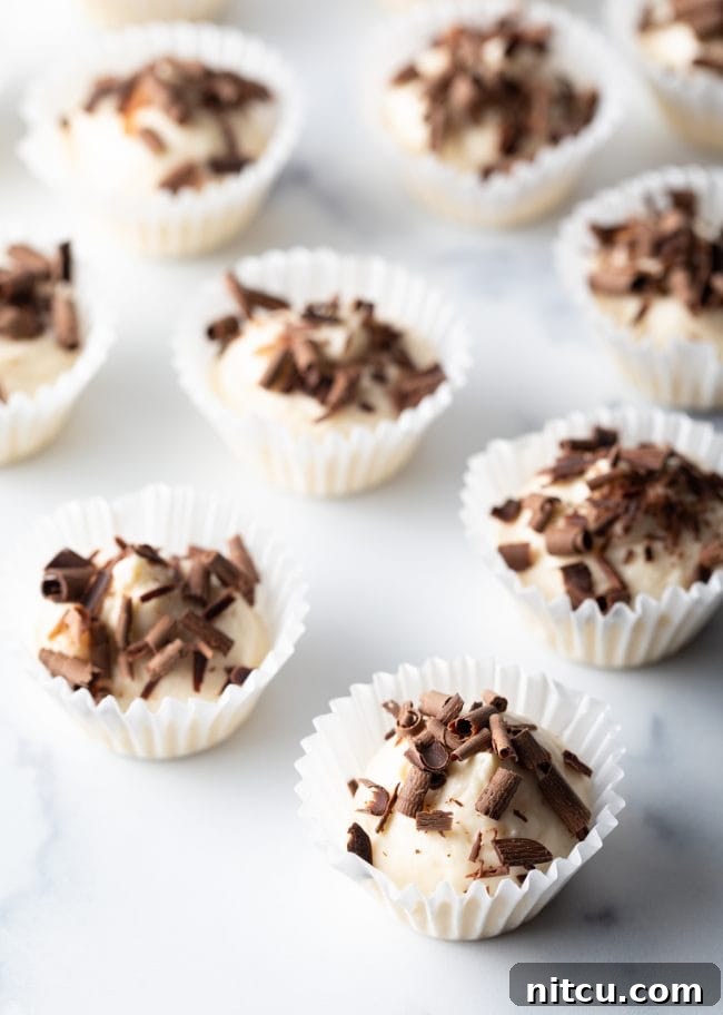 A close-up view of numerous no-bake keto fat bombs, each nestled in a small paper muffin liner and adorned with delicate chocolate shavings, highlighting their enticing texture and presentation.