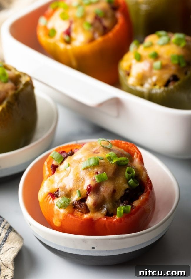 Red bell pepper stuffed with ground beef, topped with melted cheese and chopped scallions, set in a white bowl.