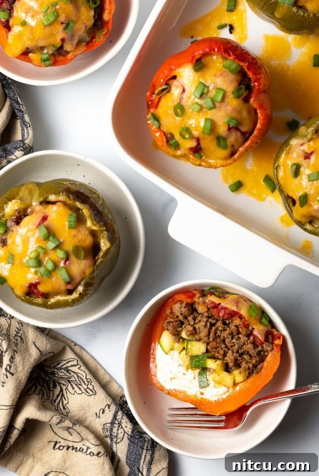 Top view keto stuffed peppers, one cut in half to show ground beef, zucchini, and cream cheese, set in a white bowl.