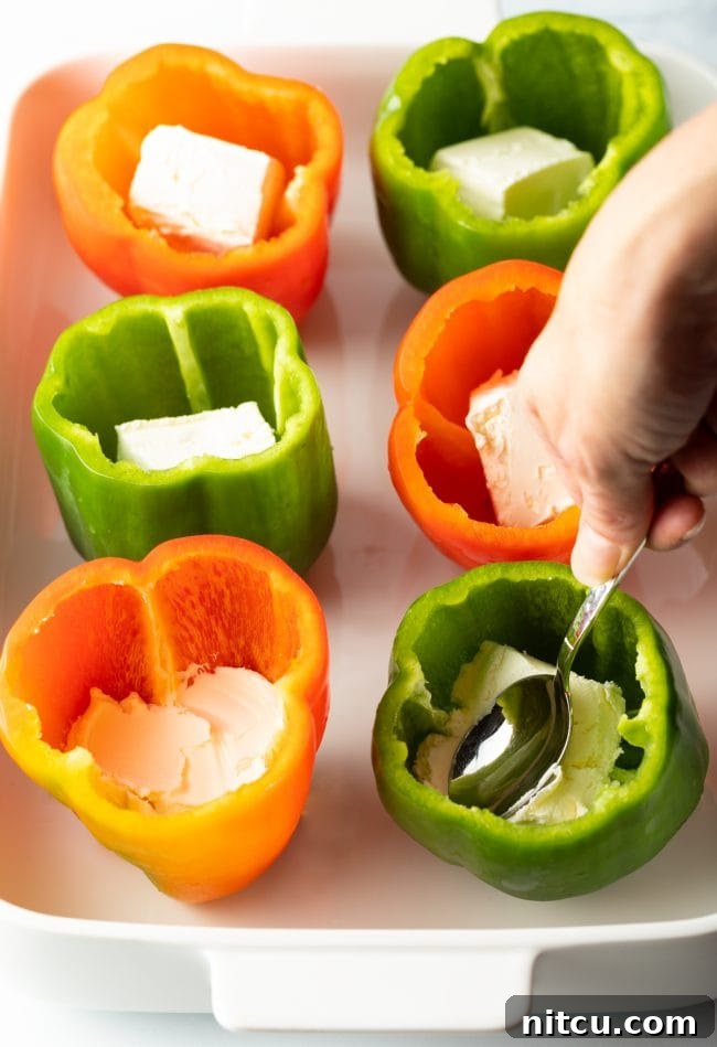 Hand using a spoon to press cream cheese into each pepper cavity.