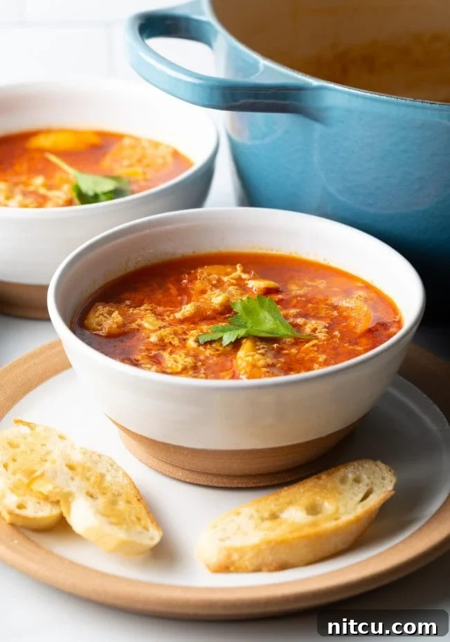 Spanish Soup (Sopa De Ajo) - close view of bowl with sopa de ajo garlic egg drop soup topped with parsley on a plate with toasted baguette