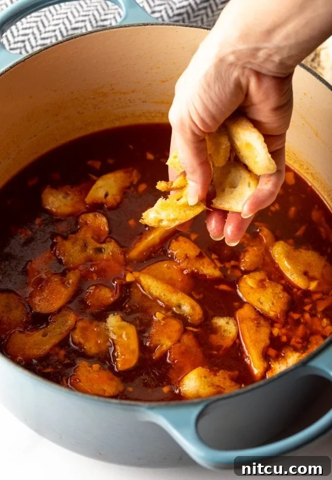 hand adding toasted baguette slices to the broth