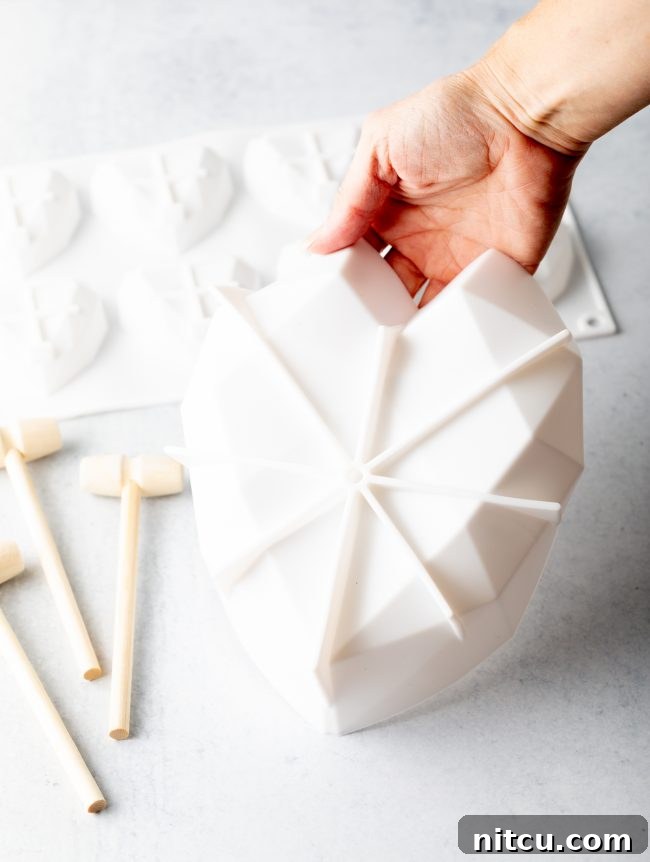 A hand gently holds a pristine white silicone heart shell mold, showcasing its perfect shape and readiness for crafting a beautiful breakable chocolate heart.