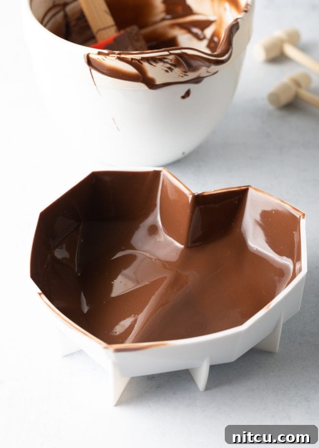 The interior walls of a heart mold are evenly coated with perfectly melted chocolate, forming a smooth, ready-to-set shell.