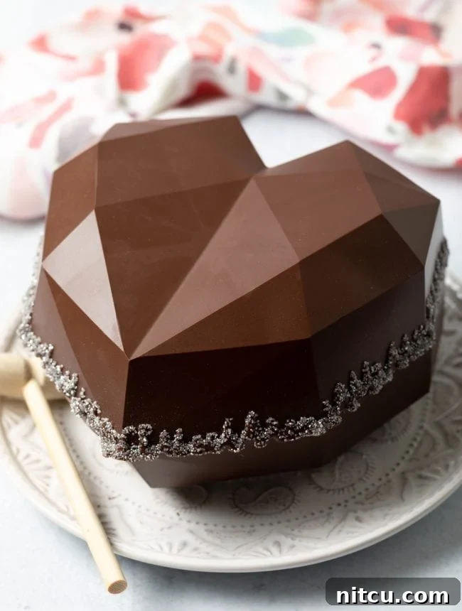 A dazzling, complete breakable chocolate heart gift box sits on a white surface, encircled by edible glitter, sparkling with festive charm.