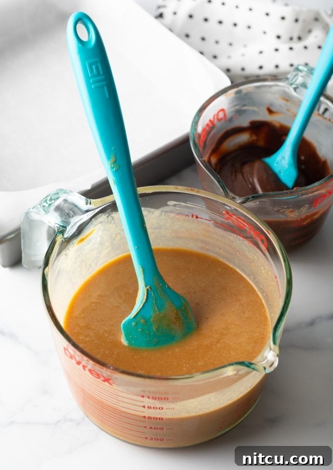 Melted peanut butter mixture in a clear glass mixing cup, ready for the next step, with a blue spatula.