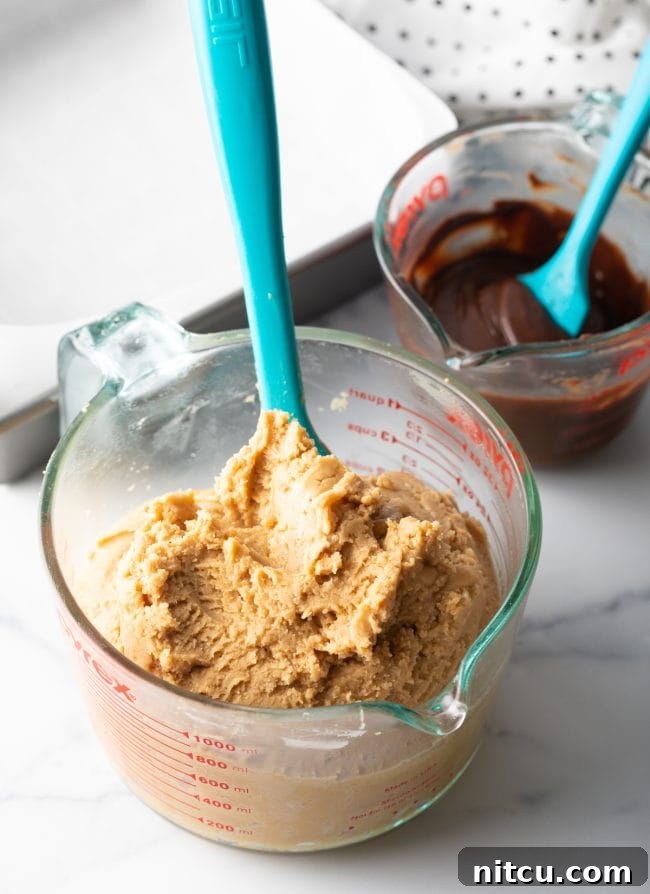 The smoothly mixed fudge base in a large glass mixing cup with a blue spatula, showing its ready consistency.