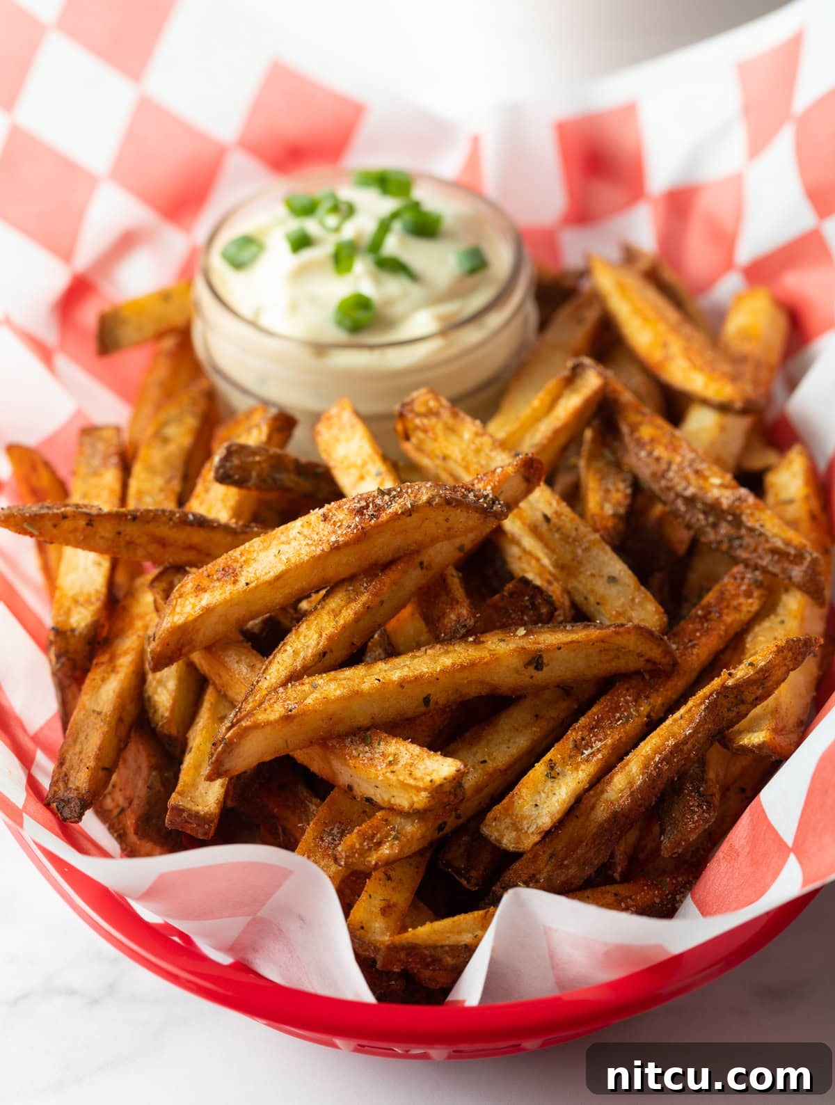 Close view of basket of seasoning fries with cup of sauce in the background.