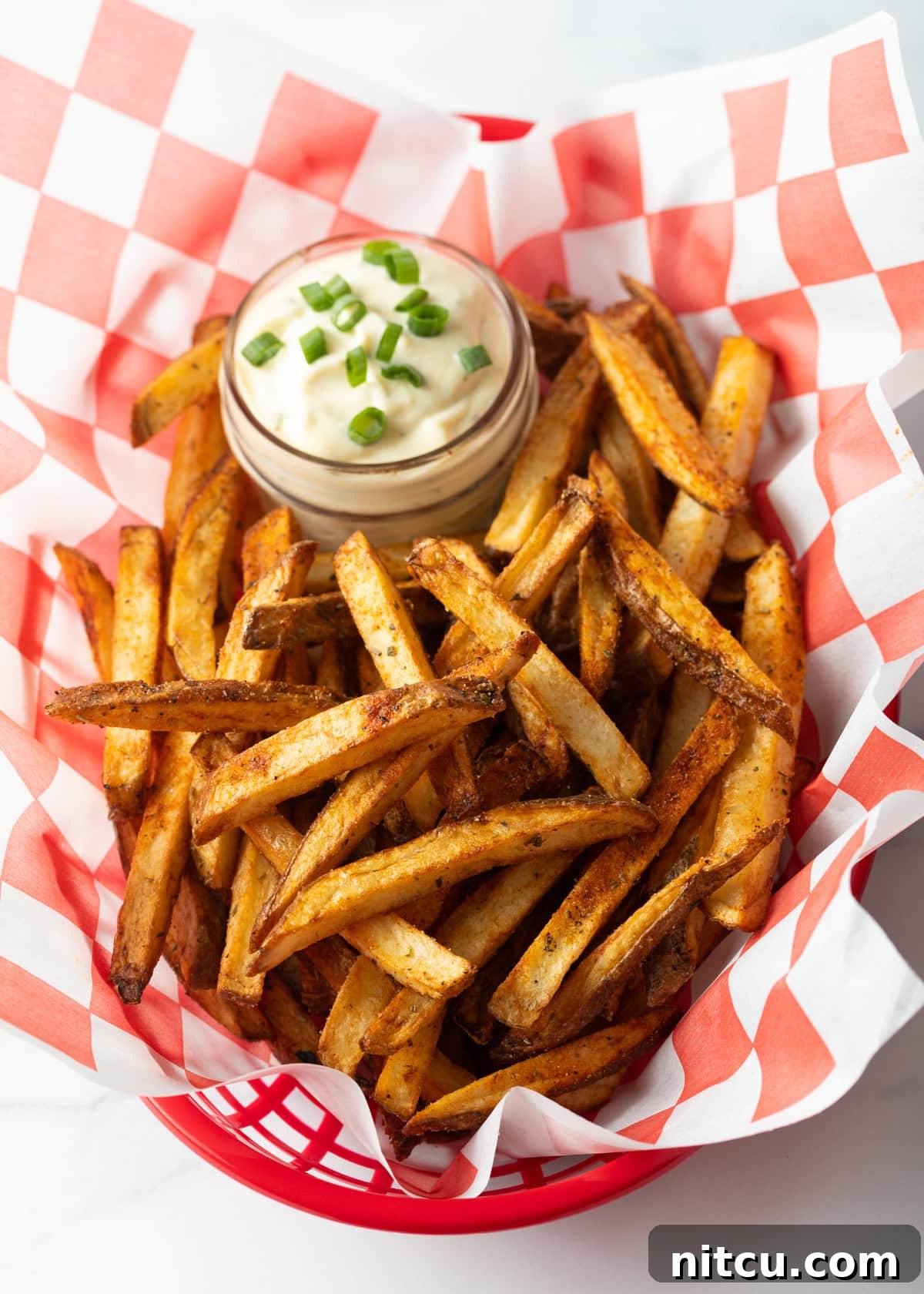 Top view Cajun seasoned fries in a basket with cup of dip.