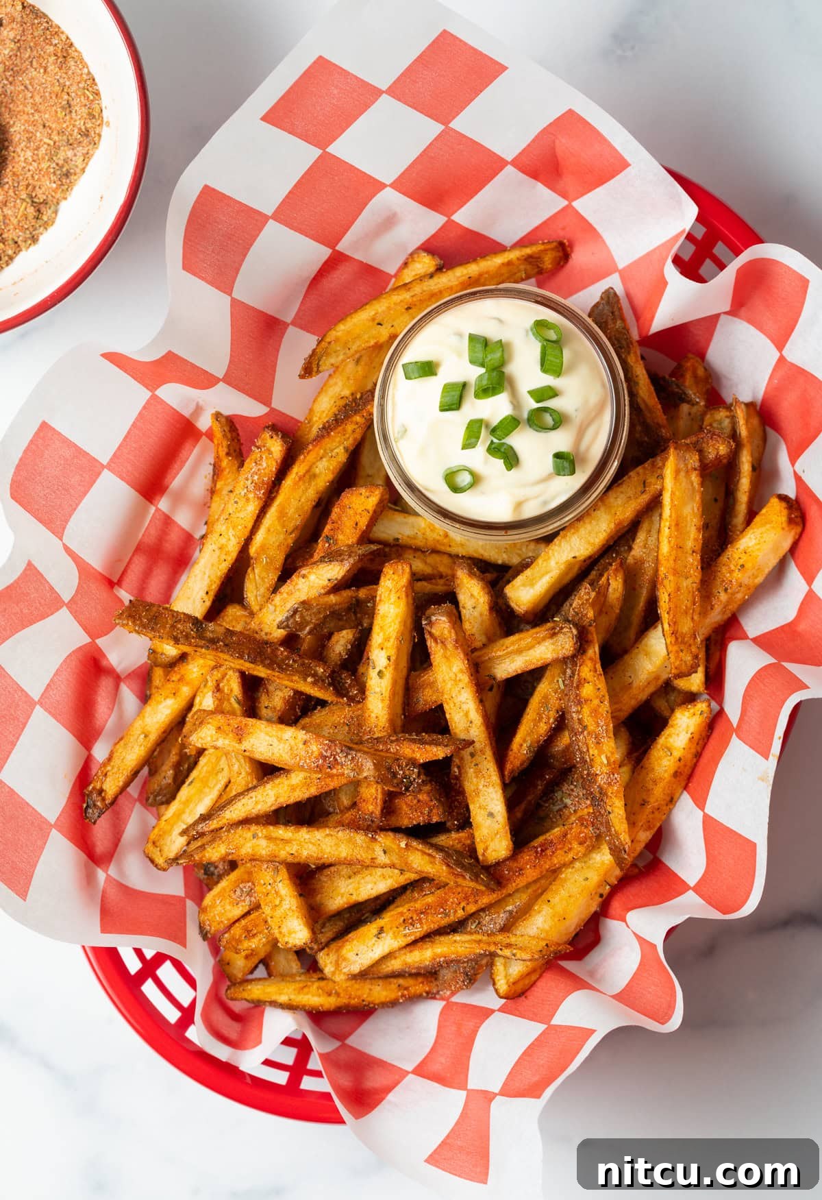 Top view spicy Cajun fries in a basket with sauce in a small cup of sauce.