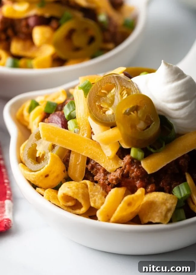 Close view of Frito chili pie in a shallow bowl, showcasing the rich chili, melty cheese, and crunchy Fritos.