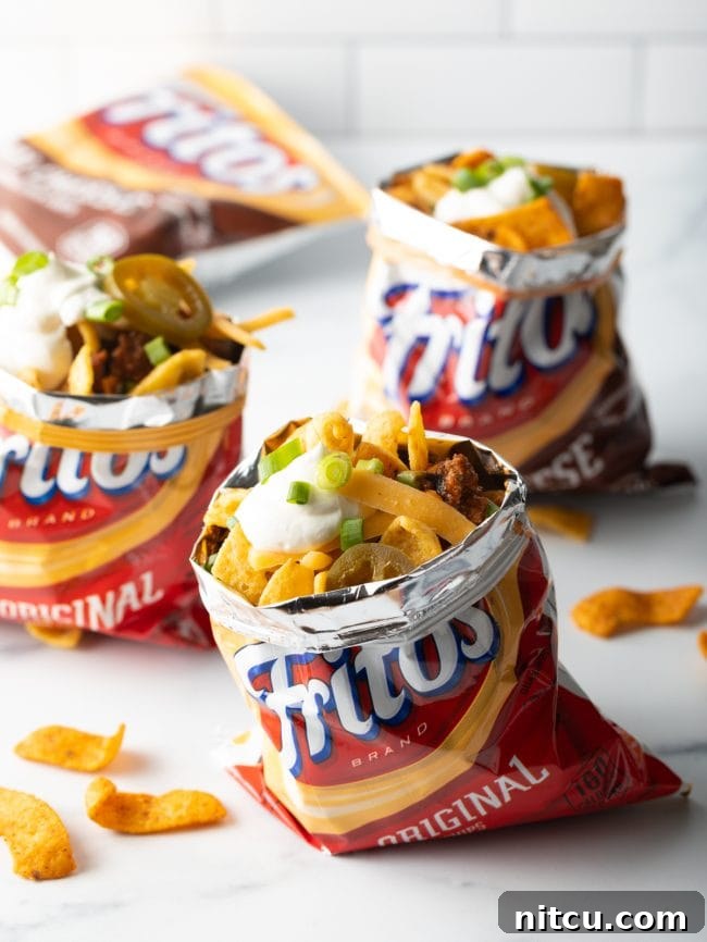 Multiple Frito corn chip bags, each generously filled with chili, melted cheese, fresh scallions, and pickled jalapenos, showcasing the portable serving style.