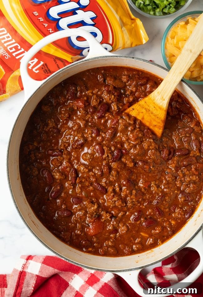 A top-down view of a finished pot of rich, simmering chili with a wooden spoon resting inside, ready for serving.