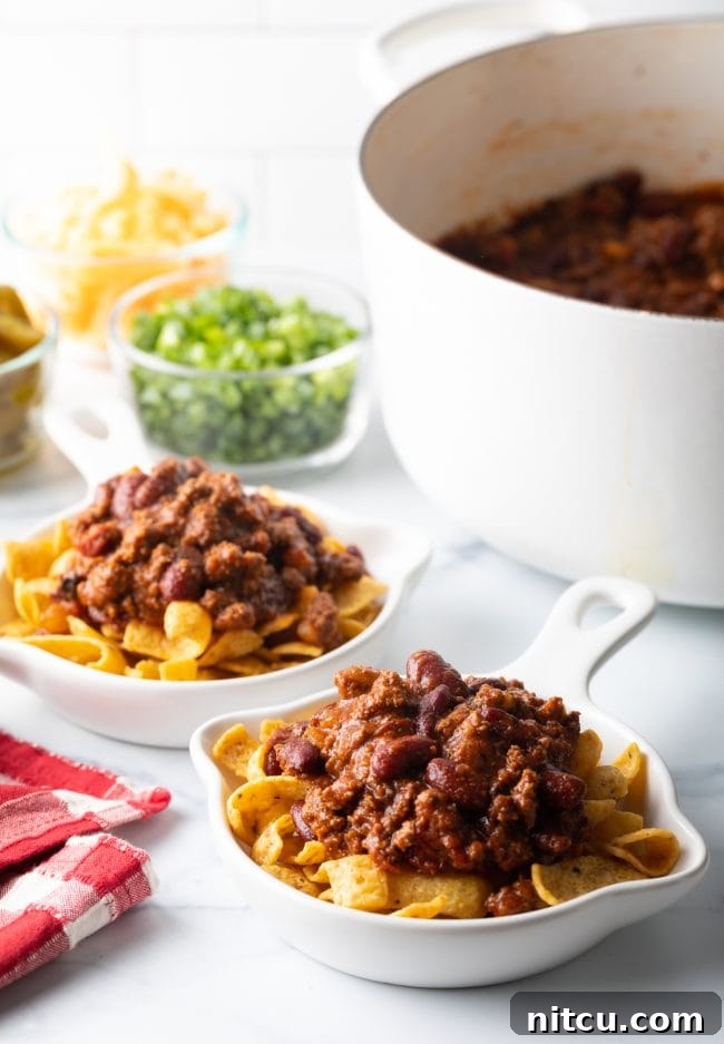 Frito corn chips forming the base in a shallow bowl, topped with a generous scoop of hot, savory chili.