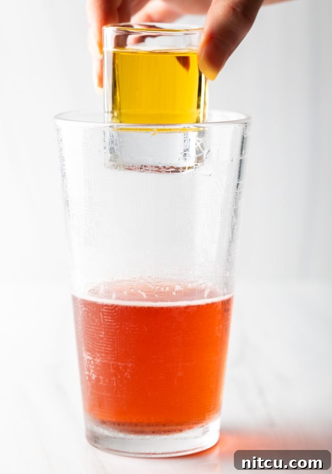 A hand holds a red bull shot above the glass for Vegas Bomb. 