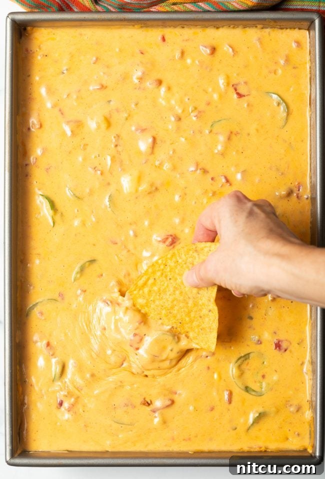 Top view of smoked queso dip in a metal pan, a hand is dipping a tortilla chip into the cheesy goodness.