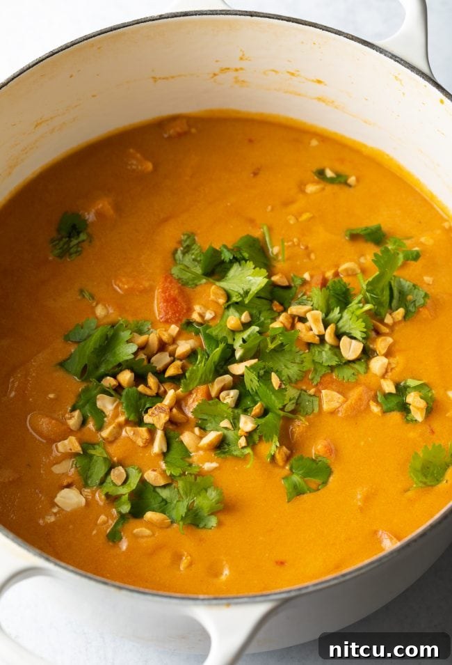Finished Maafe soup in a pot, topped with fresh cilantro and crushed peanuts, ready to be served.