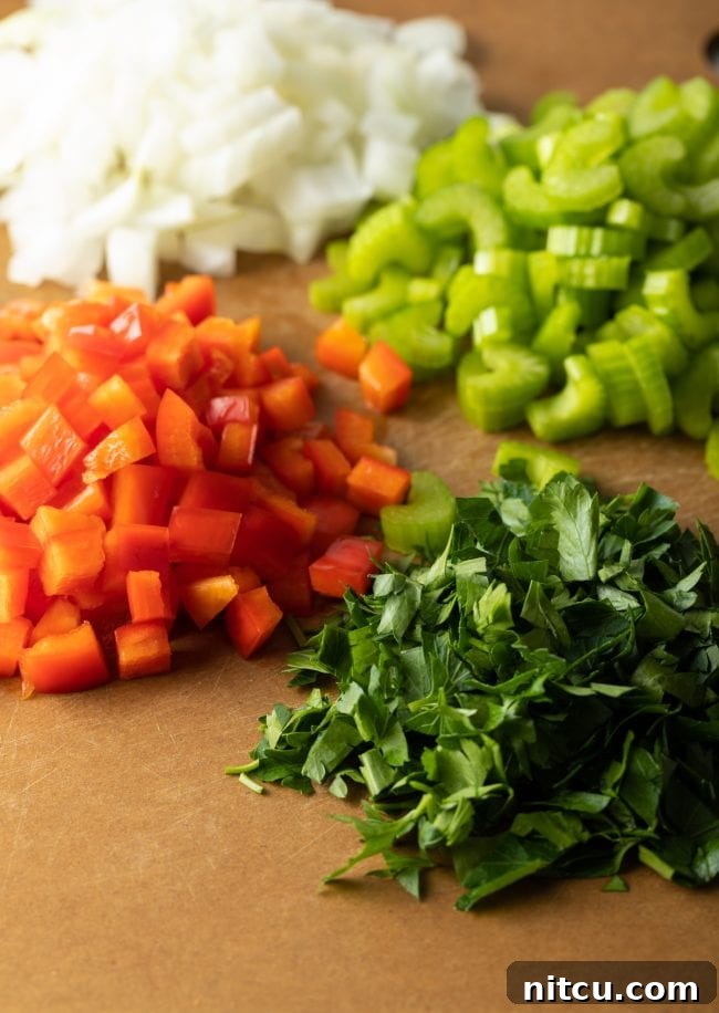 Chopped fresh ingredients including onion, celery, and bell pepper on a cutting board.