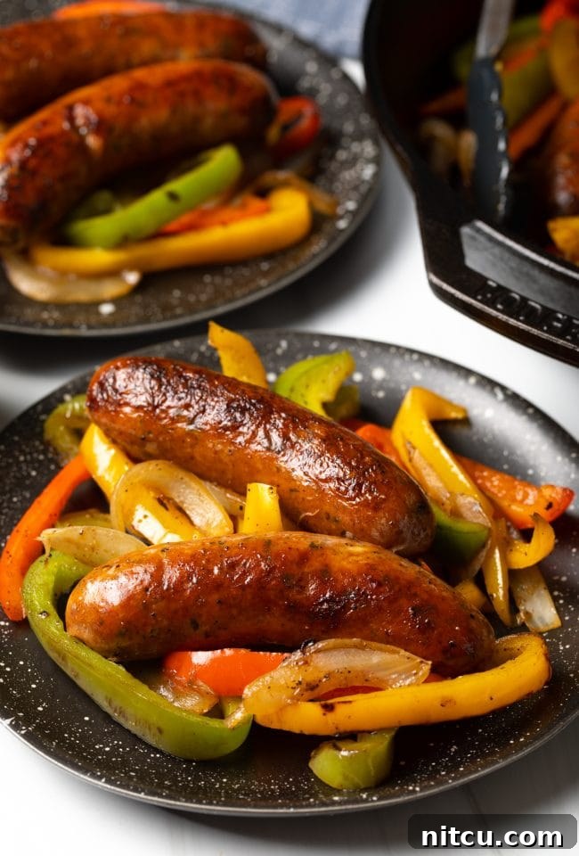 Side view two cooked sausage links with bell peppers and onions on a plate.