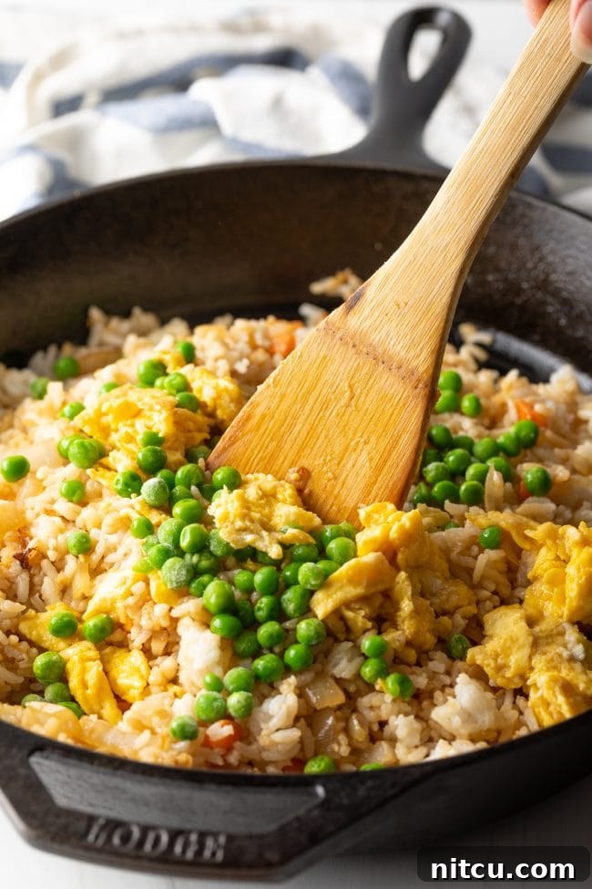 A spatula combining fluffy rice and colorful veggies, ensuring even coating.