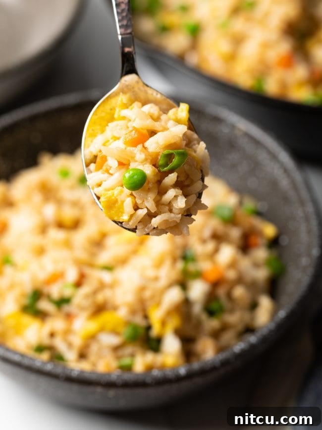 Spoonful of hibachi rice with eggs and veggies held towards camera, showcasing its texture.