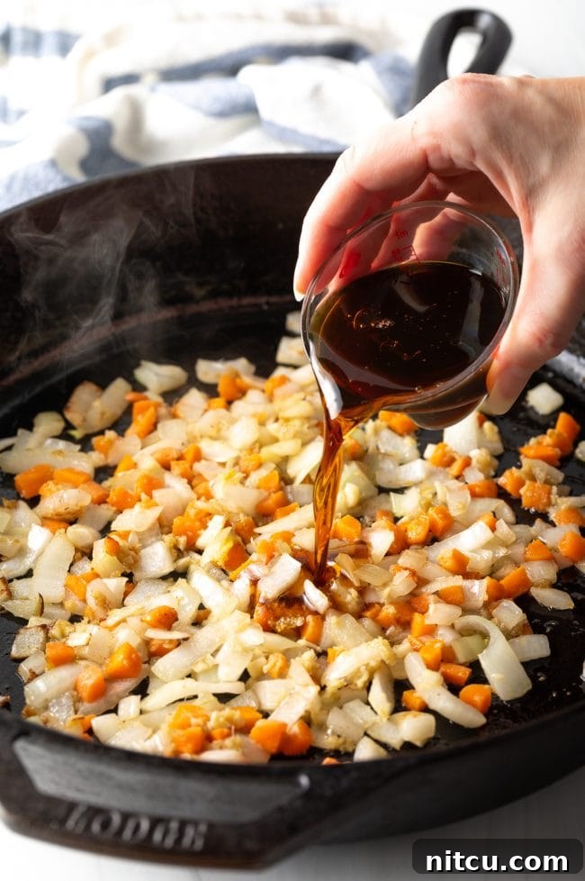 A hand pouring savory sauces over sautéed vegetables, creating a rich aroma.