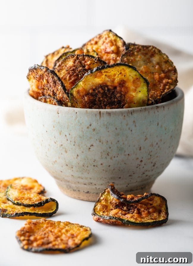 A speckled bowl overflowing with fried zucchini chips, with several chips playfully scattered around the bowl on a wooden surface.