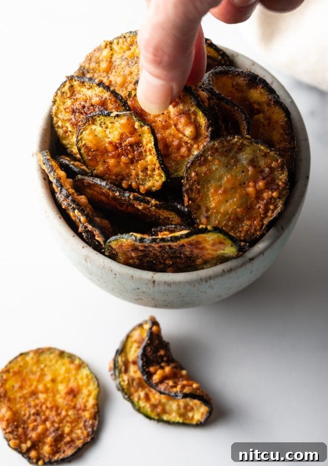 Top down view of a hand reaching into a bowl filled with golden-brown air-fried zucchini chips.