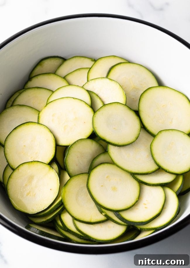 A bowl filled with freshly sliced zucchini rounds, showing some moisture release after salting.