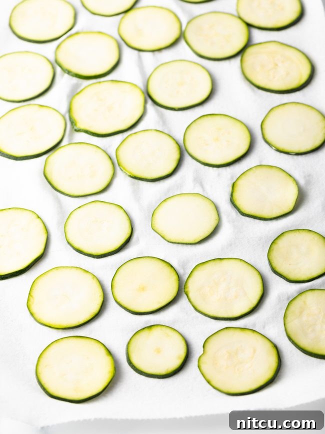 Raw, thinly sliced zucchini laid out in a single layer on a paper towel, ready for patting dry.