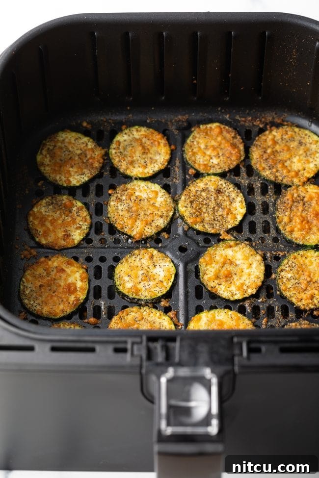 Golden-brown zucchini slices fried in an air fryer, generously topped with melted parmesan cheese, ready to be served.
