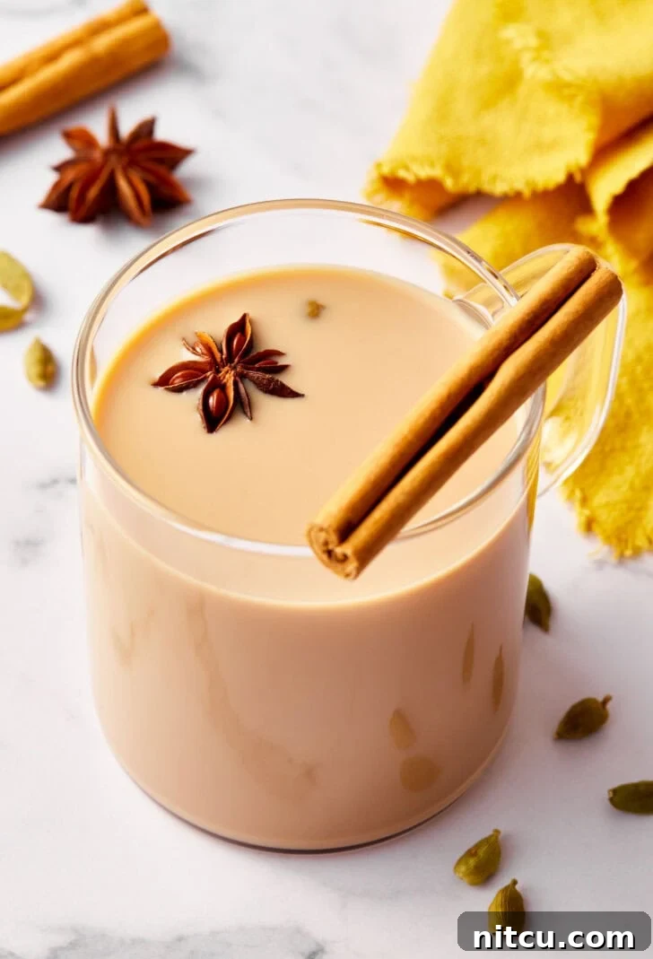 Closeup of chai tea in a clear glass mug, elegantly garnished with a cinnamon stick and a star anise, highlighting its rich aroma.
