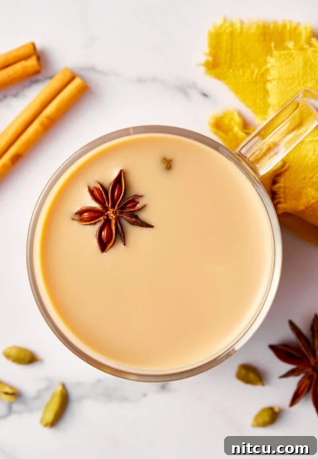 Top-down view of a clear mug filled with foamy chai tea, garnished with a sprinkle of warming spices, highlighting its inviting aroma.