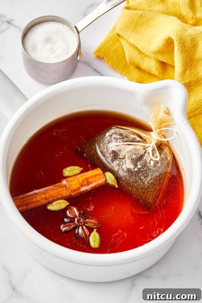 Best Chai tea steeping in a large stock pot with cinnamon sticks, star anise pods, and cracked cardamom pods, infusing deeply aromatic flavors.