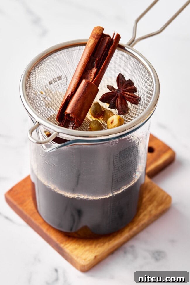 Straining freshly brewed chai tea concentrate into a pitcher, separating the rich liquid from the infused spices and tea leaves.