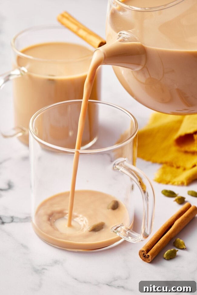 Pouring a freshly made, creamy chai latte into a clear glass mug, ready to be enjoyed.