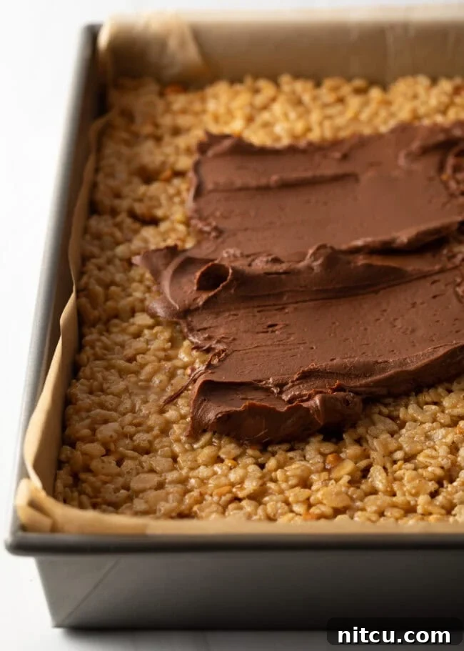 Spreading chocolate ganache on top of pressed cereal treats in a pan.