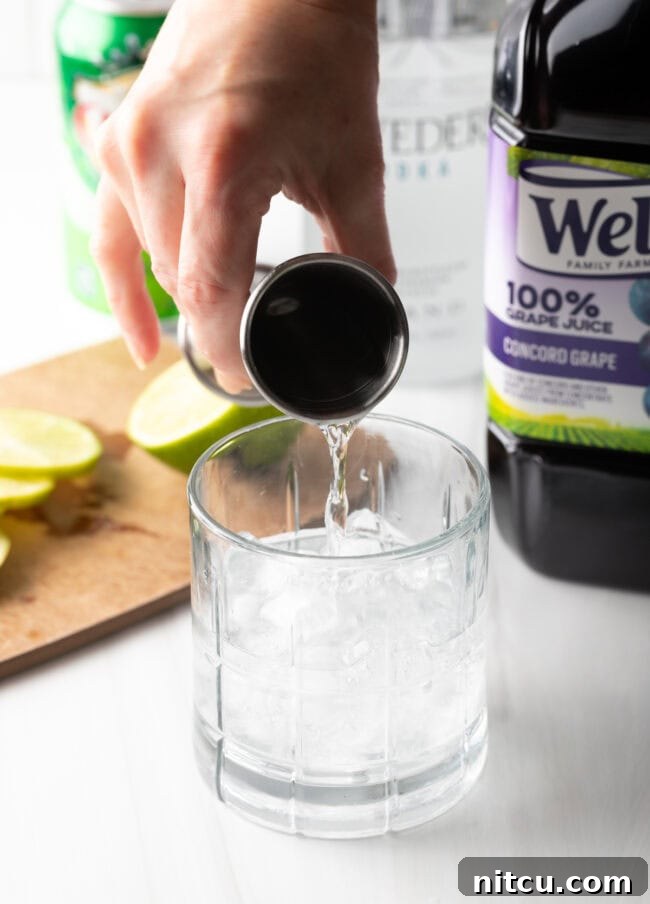 A hand pouring vodka from a jigger into a glass filled with ice.