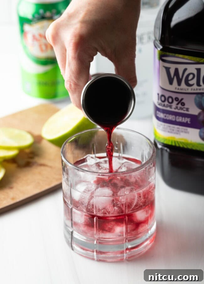 A hand pouring purple grape juice into a glass with ice and vodka.