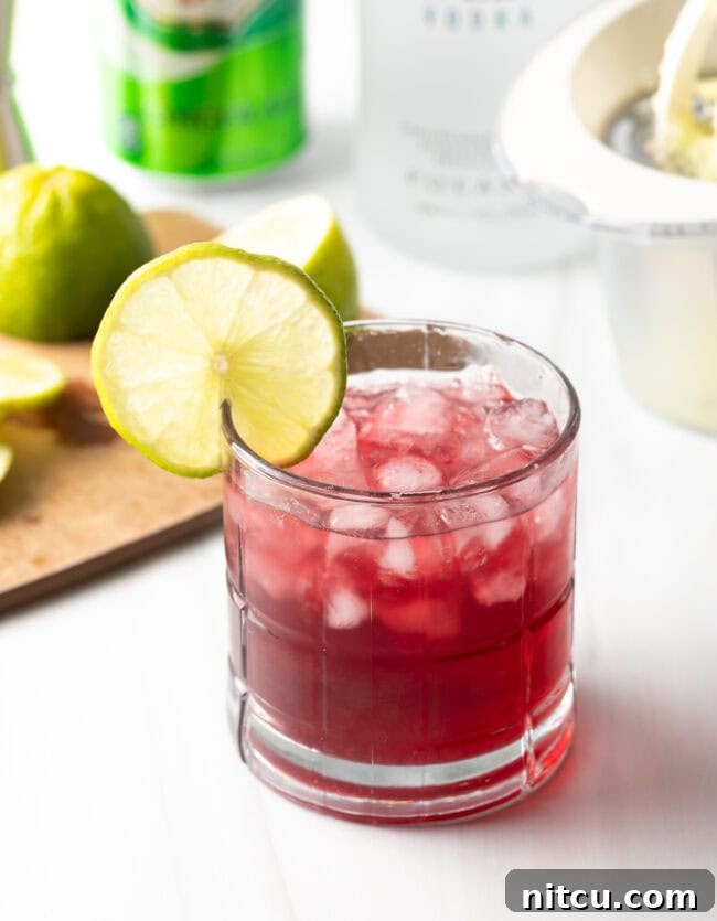 A vibrant cocktail in a tall glass with a lime garnish, against a soft, inviting background.
