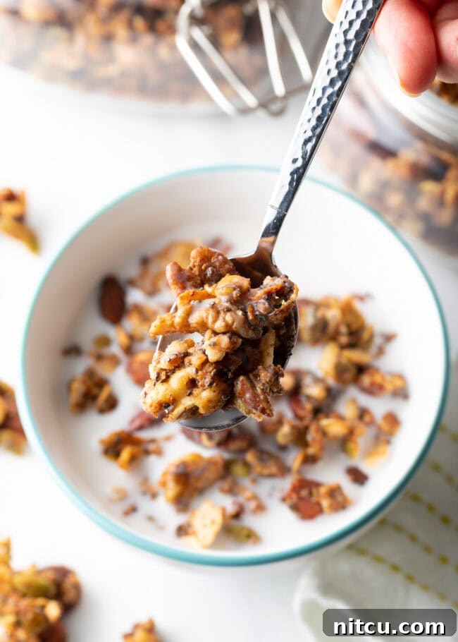 Top view of a spoon with granola and milk held towards the camera, above a bowl of granola.
