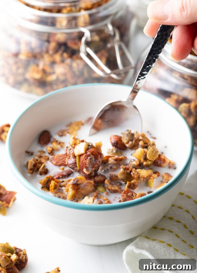 Bowl with keto granola and milk, with a hand scooping the granola with a spoon.