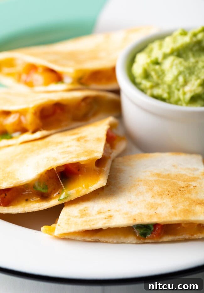 Pieces of shrimp quesadilla on a plate, with a small bowl of guacamole. 