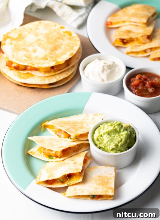 Full spread of shrimp quesadillas on plates, stacked in background, ramekins of guacamole, sour cream, and salsa.