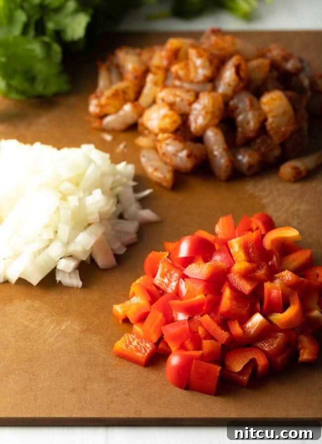 Piles of chopped ingredients on a cutting board: shrimp, onion, red bell pepper.