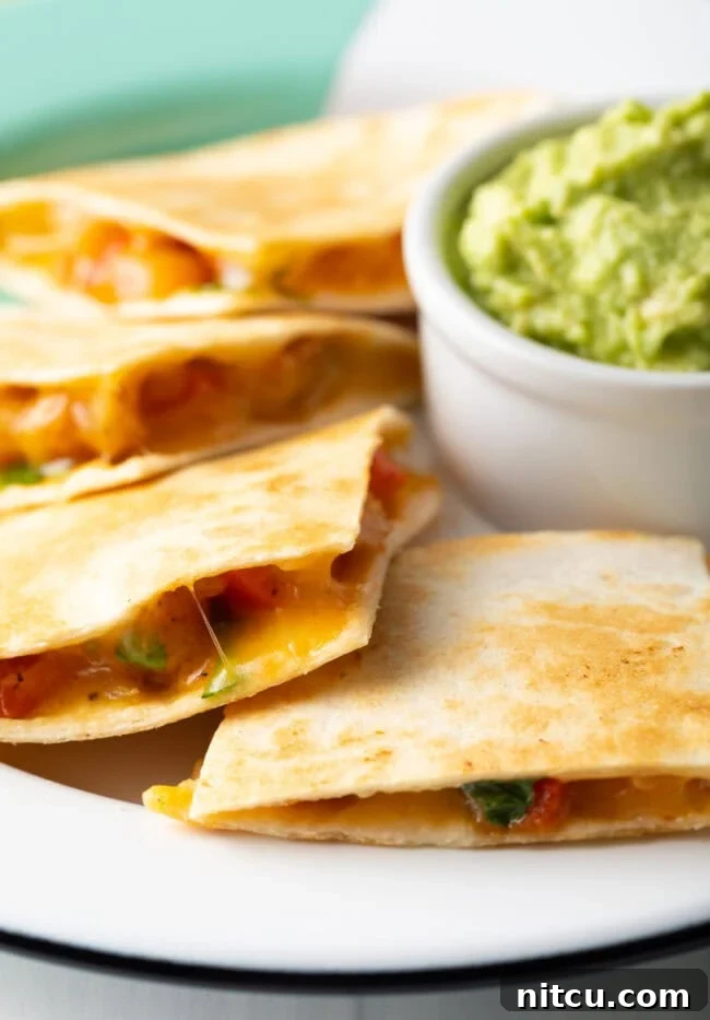 Closeup view of slices of shrimp quesadilla ontop of plate with guacamole filled ramekin in the background. 